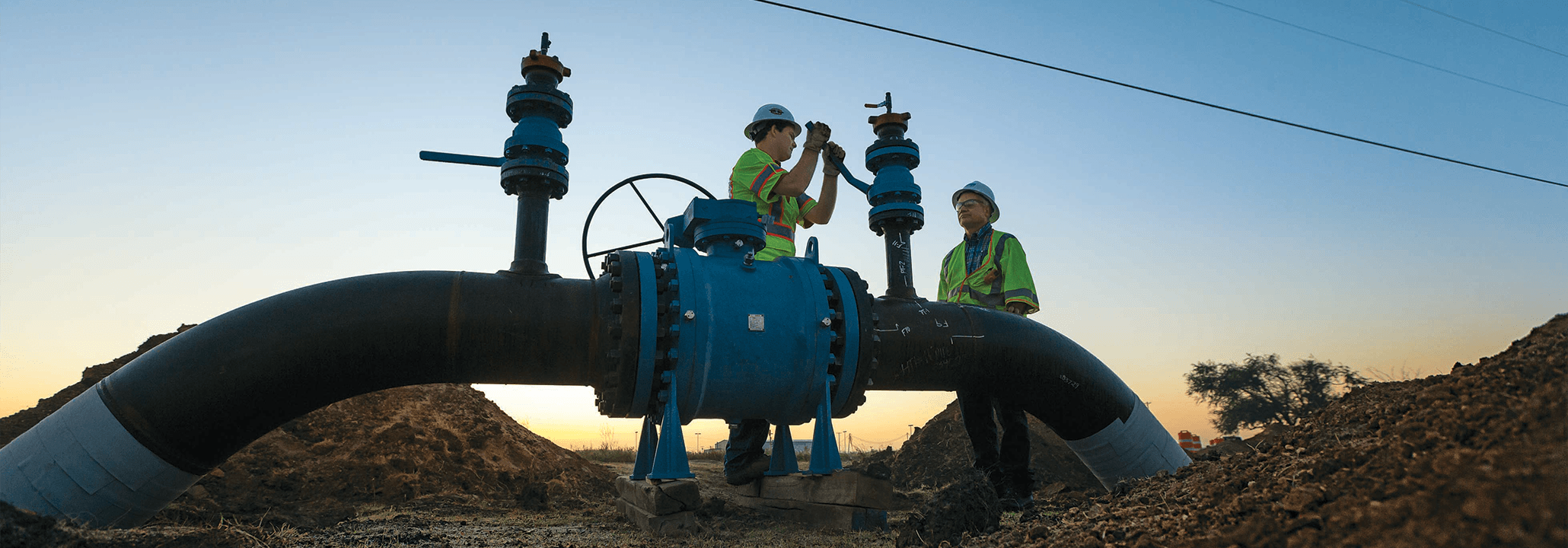 Two Atmos Energy employees working on large pipelines at dusk